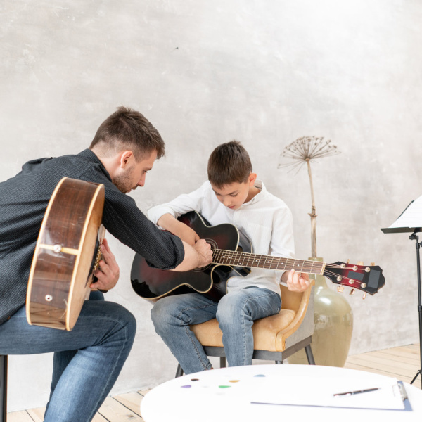 student playing the guitar during a music lesson with a guitar teacher guiding them