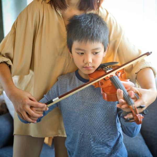 student learning the violin with the help of a teacher during a lesson